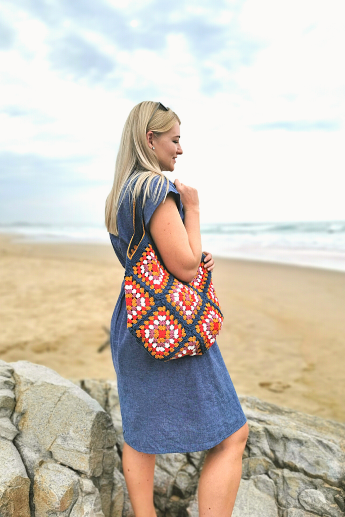 woman standing on beach holding granny square tote bag