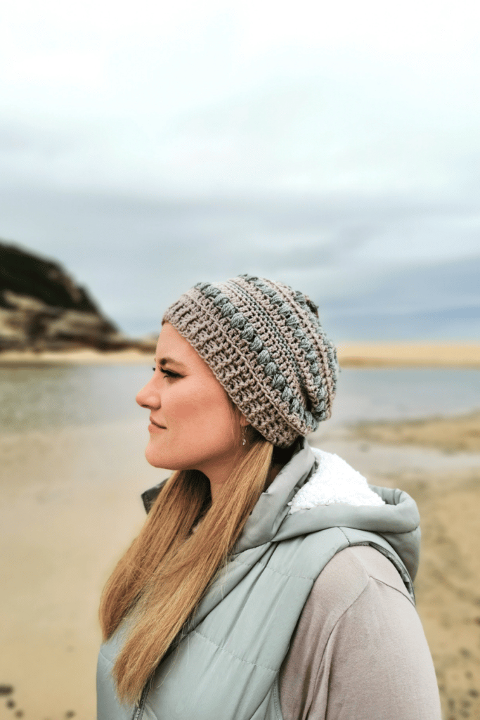 a woman wearing a sand and sage color slouchy hat standing in front of the ocean