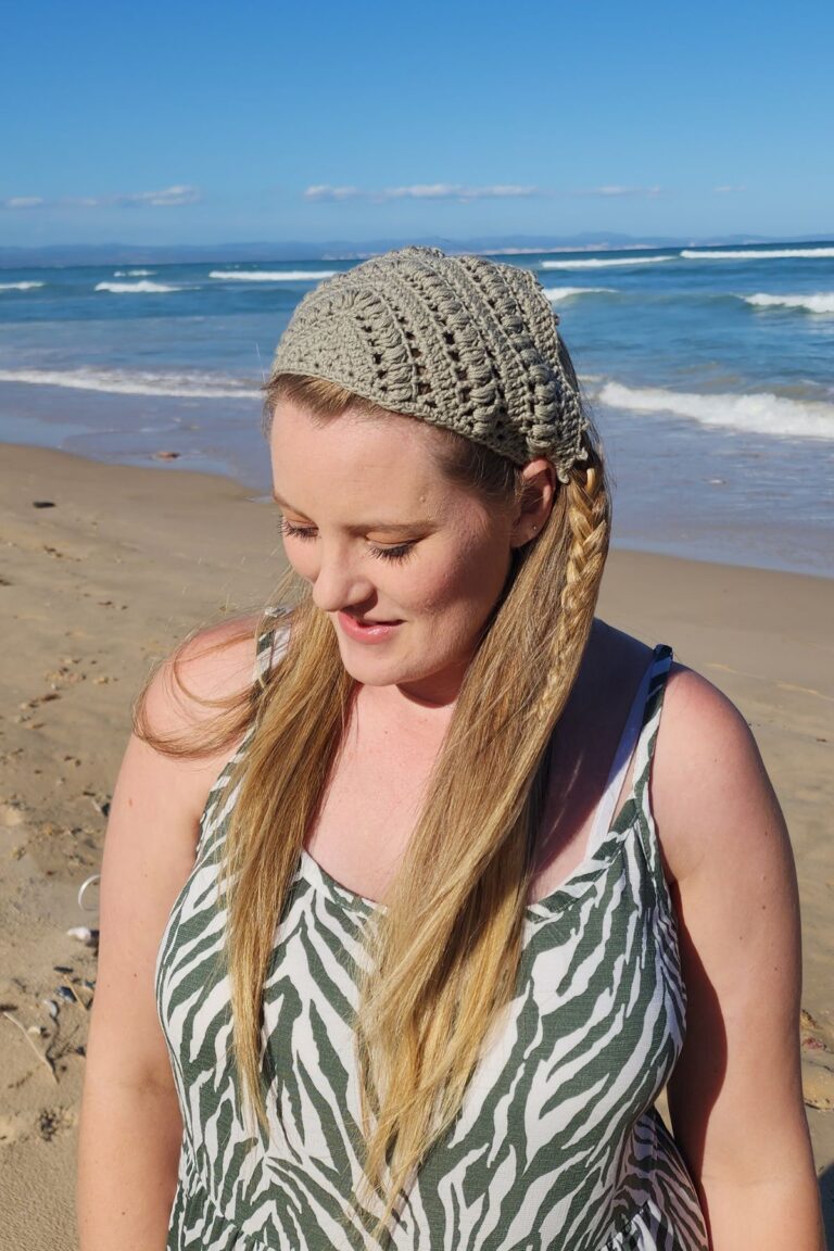 A photo of a woman standing in front of the ocean wearing a crochet bandana